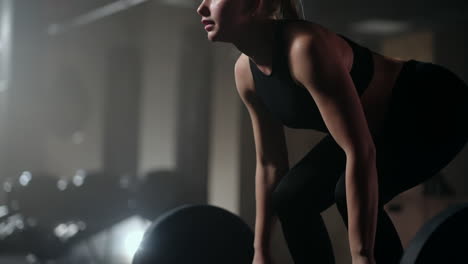 Slow-motion:-A-woman-lifts-a-barbell-in-a-dark-gym-with-a-lot-of-weight.-A-strong-young-woman-lifts-weights-for-a-workout